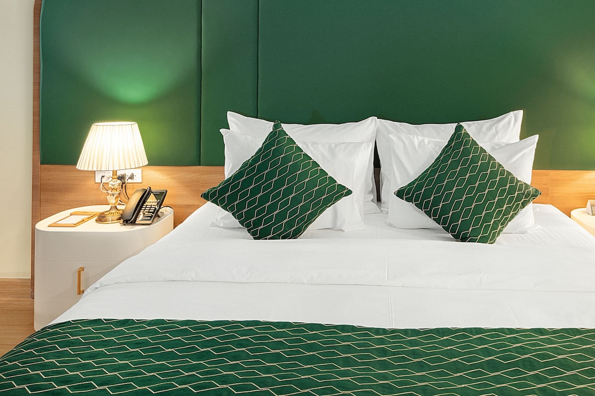 Un lit bien fait, avec une couvre-lit à motifs verts et des oreillers, deux lampes de chevet et une tête de lit en bois.