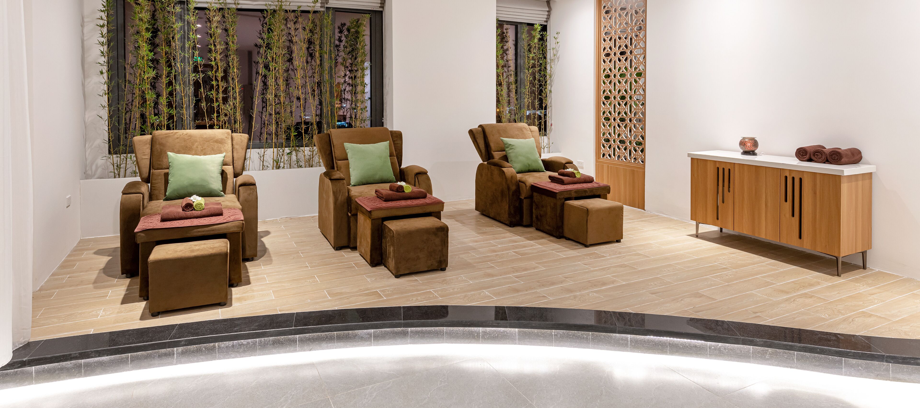 A spa room with three reclining chairs, a wooden cabinet, and a window with bamboo plants.