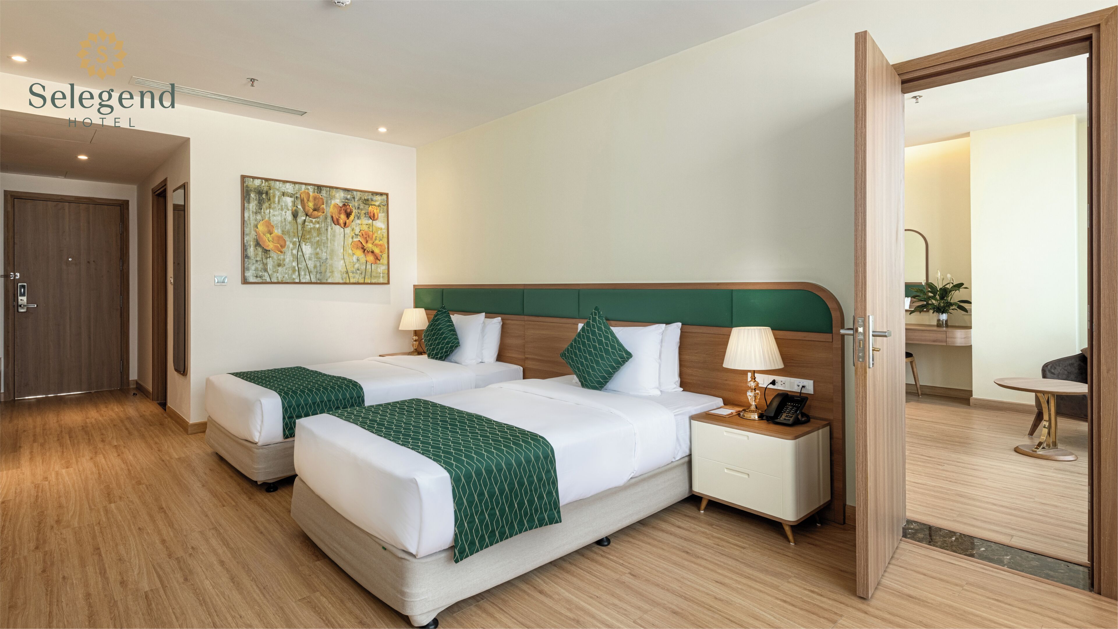 A hotel room with two beds, a nightstand with a lamp, a painting on the wall, and a wooden floor.