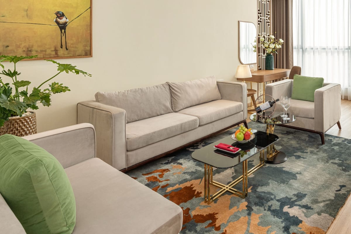 Un salon moderne avec un canapé, une table basse et des fauteuils. Un tableau orne le mur, un vase rempli de fleurs est posé sur une table, et une fenêtre est agrémentée de rideaux légers.