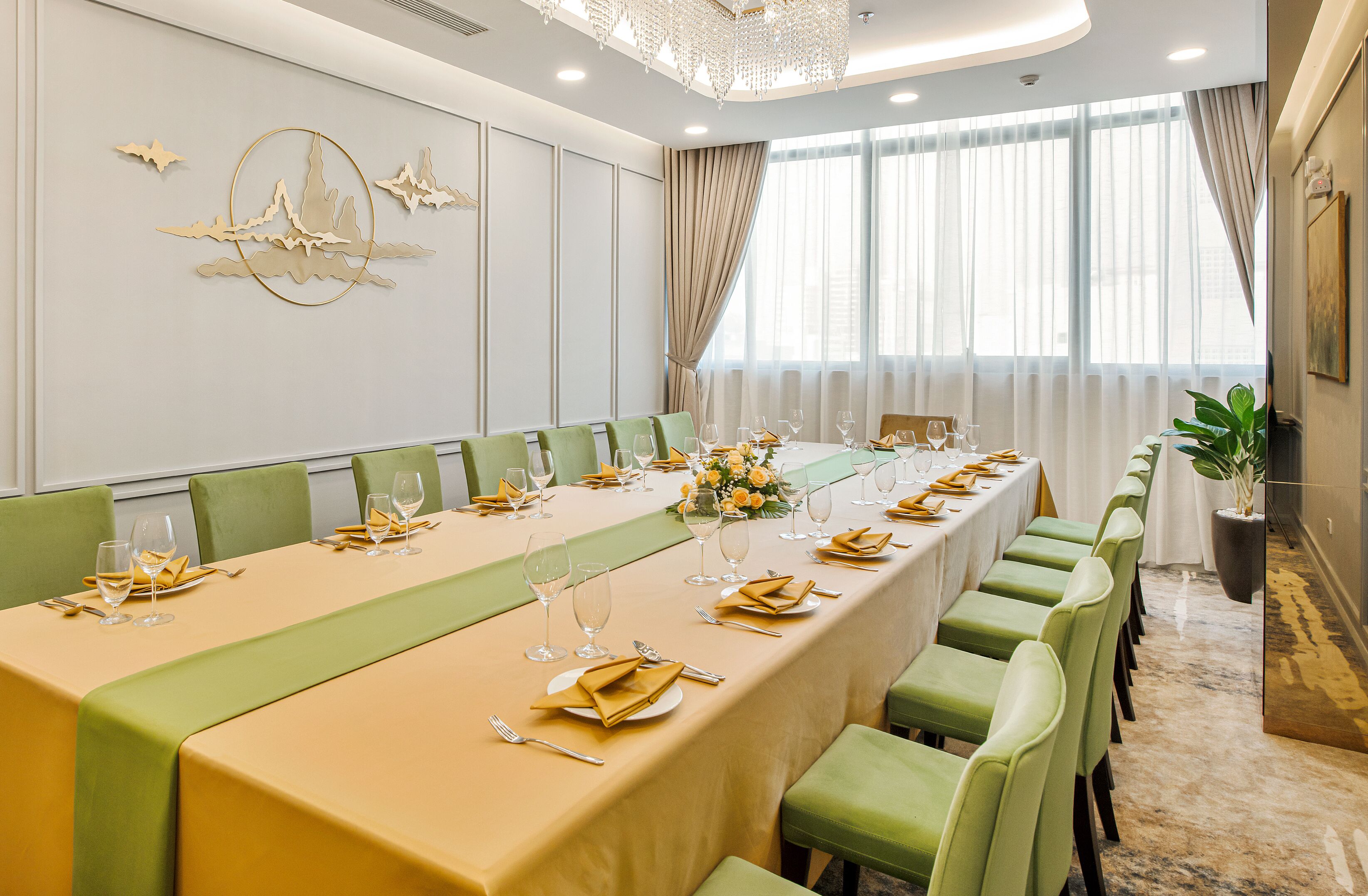 A conference room with a long table set for a meeting, green chairs, and a chandelier.