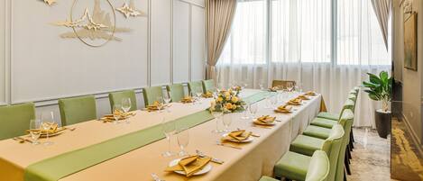 A conference room with a long table set for a meeting, green chairs, and a chandelier.