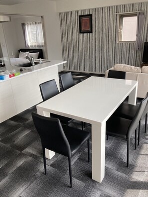 A modern dining area with a white table and black chairs, a kitchen area with a sink and countertop, and a striped wall with a picture frame.