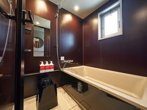 Ein modernes Badezimmer mit einer großen Badewanne, einer Dusche und einem Waschtisch mit Spiegel und Pflegeprodukten.