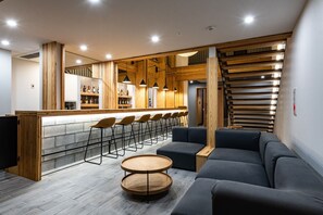 A modern bar area with wooden accents, a seating area with sofas and round tables, and a visible bar counter with stools.