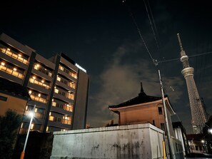 Un bâtiment moderne à plusieurs étages, doté de grandes fenêtres illuminées, une pagode traditionnelle et une tour imposante en arrière-plan.