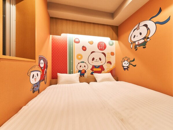 Une chambre d’hôtel avec un lit, des oreillers, un mur décoré de personnages de dessins animés et une fenêtre avec des stores.