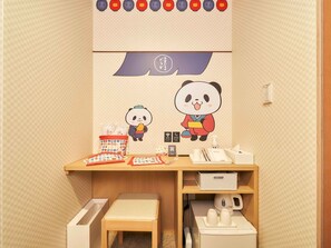 A child's room with a desk, a panda-themed wall decoration, a small stool, and a white kettle.