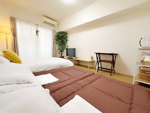 Una camera d'albergo con due letti, una scrivania, una televisione e una pianta.