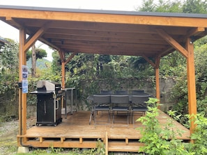An outdoor covered patio with a grill, seating area, and a wooden deck.