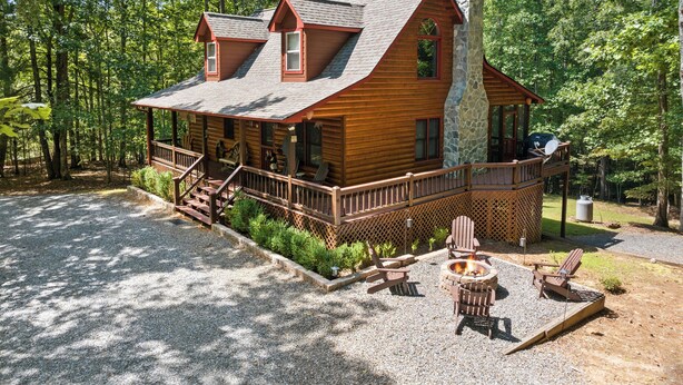 Une cabane en rondins avec une cheminée en pierre, une terrasse dotée de fauteuils Adirondack et un foyer extérieur.