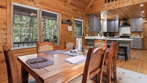 L’intérieur d’une cabane en bois comprend une table à manger, des chaises, un coin cuisine et de grandes fenêtres.