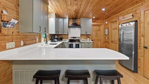 Une cuisine moderne avec un lambris en bois, un grand îlot central doté de tabourets, des appareils électroménagers en acier inoxydable et une hotte aspirante au centre.