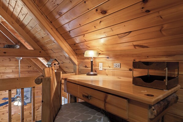A wooden cabin interior with a desk, lamp, and a cat on the ceiling. - The Cabin, Hot Tub, Game Room, Screened Porch, Fire Pit (Morganton)