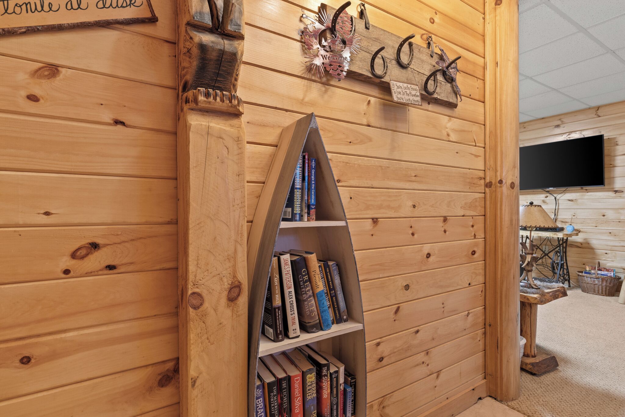 A wooden interior with a bookshelf, a welcome sign, and a television mounted on the wall.