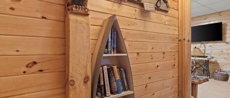 A wooden interior with a bookshelf, a welcome sign, and a television mounted on the wall.