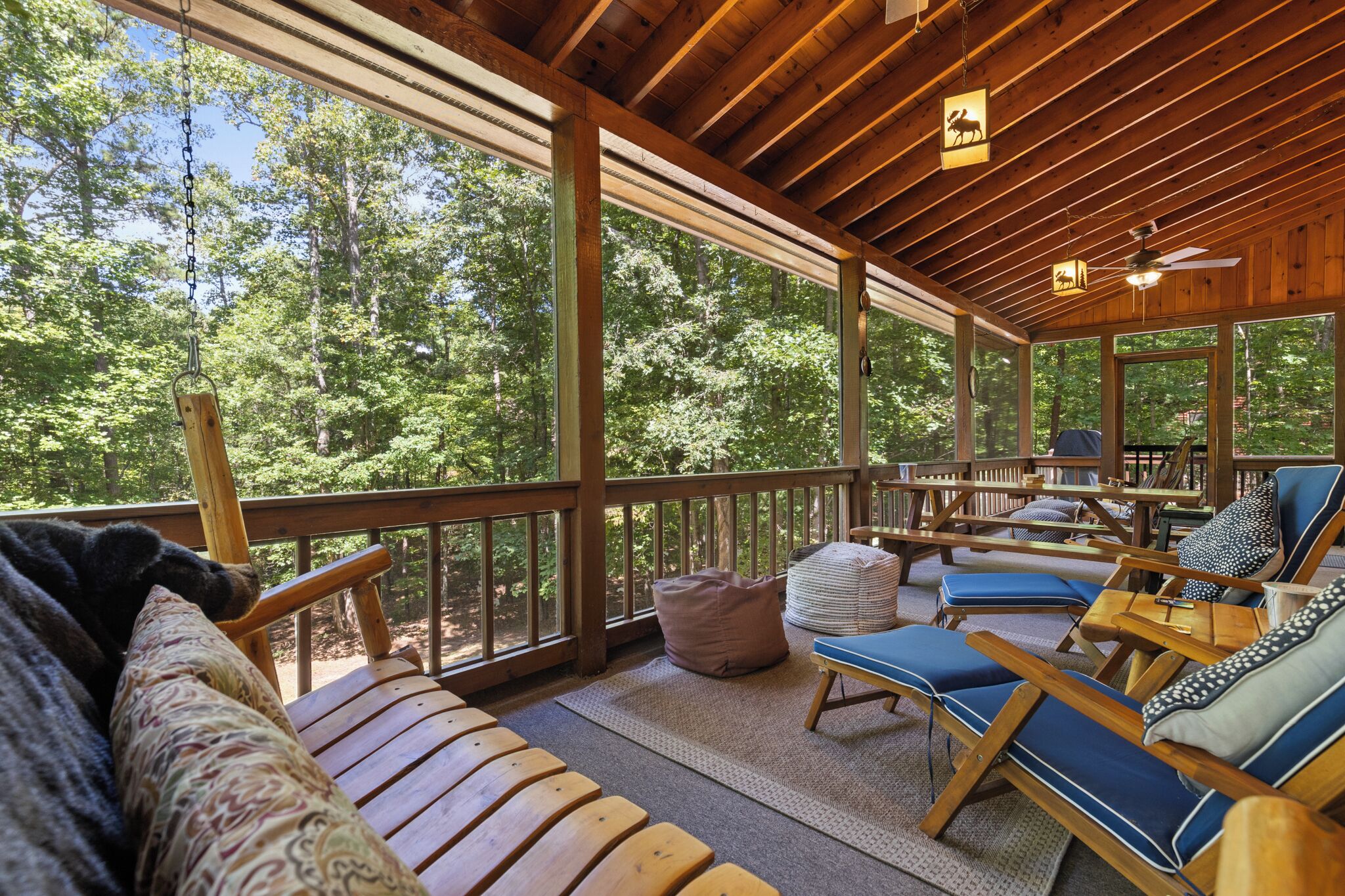 Una terrassa de fusta amb seients exteriors, grans finestres i un ventilador de sostre.