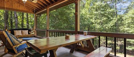 A wooden deck with a picnic table and benches, surrounded by large windows offering a view of a forest.