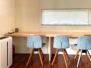 Quarto com escrivaninha de madeira, três cadeiras estofadas em azul, aquecedor branco e janela com persianas.