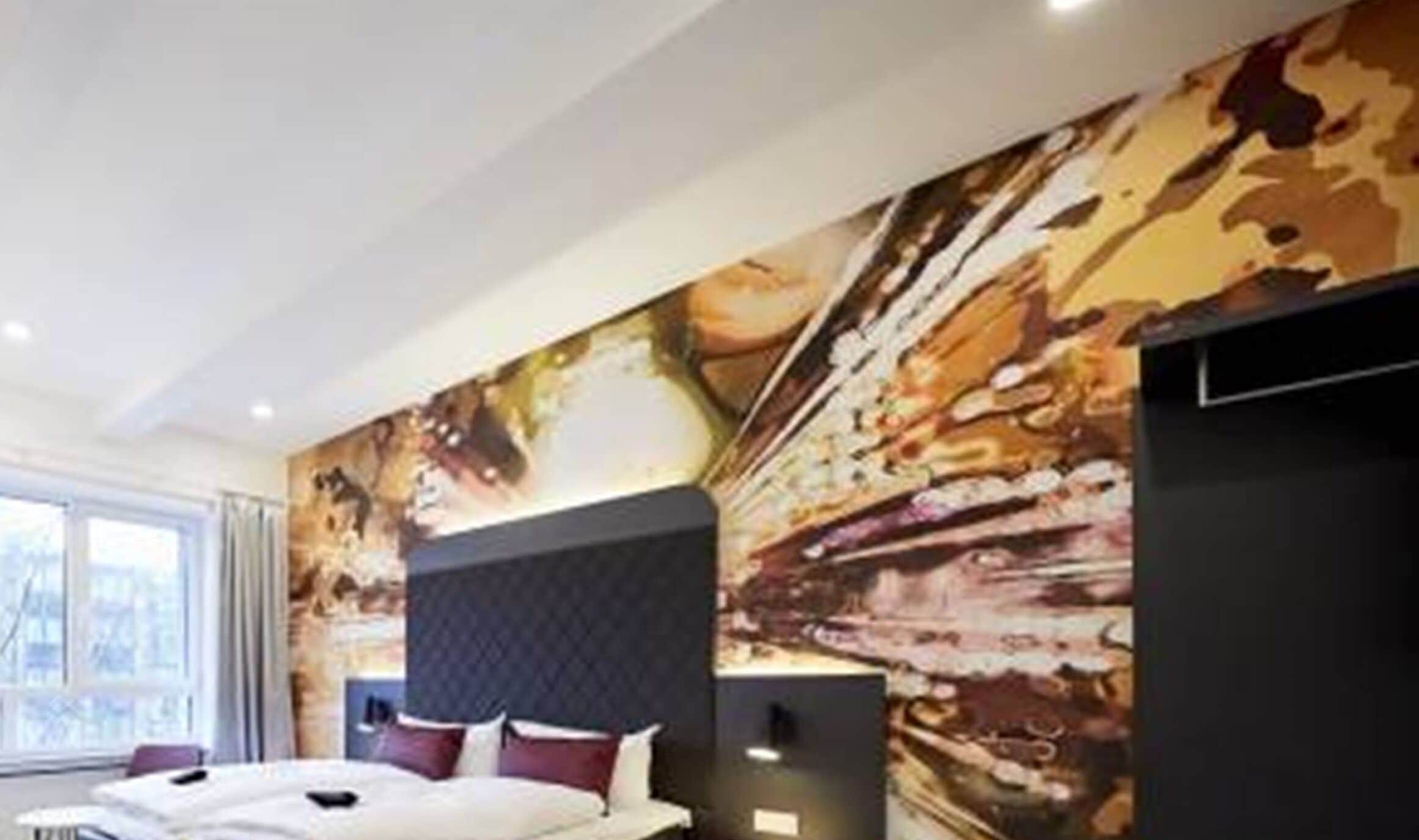 A modern hotel room with a large bed, a headboard, and a wall mural.