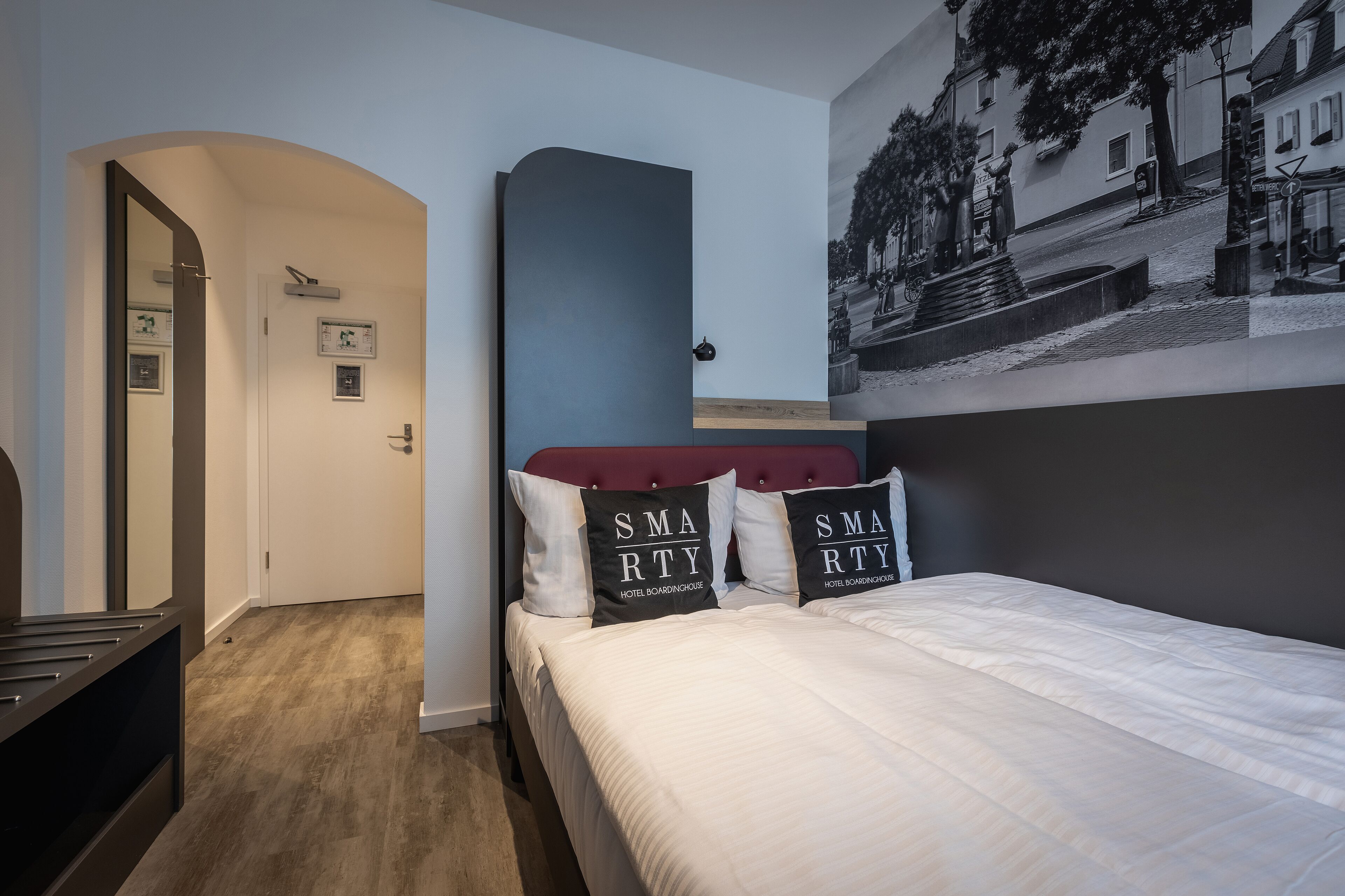 Una habitación de hotel con una cama, cabecera roja y un cuadro colgado en la pared.