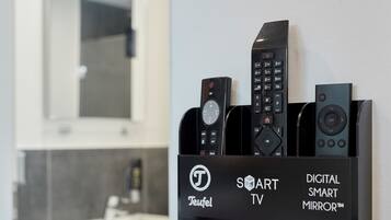Un mueble de pared para televisor con varios controles remotos, un espejo y un letrero que indica que es un televisor Teufel Smart con un Espejo Inteligente Digital.