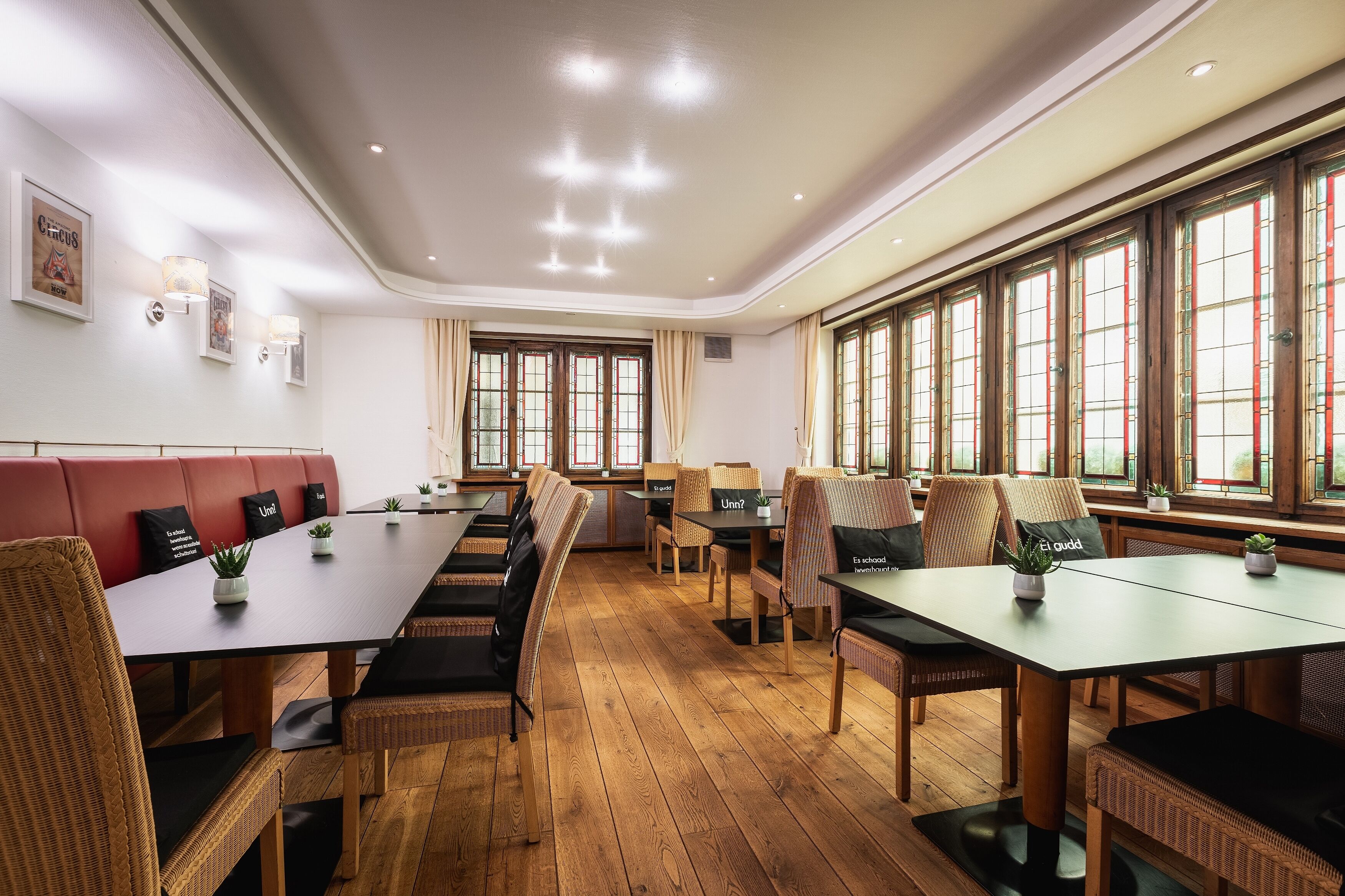 A spacious dining area with long tables and wicker chairs, large windows with curtains, and wall-mounted lights.