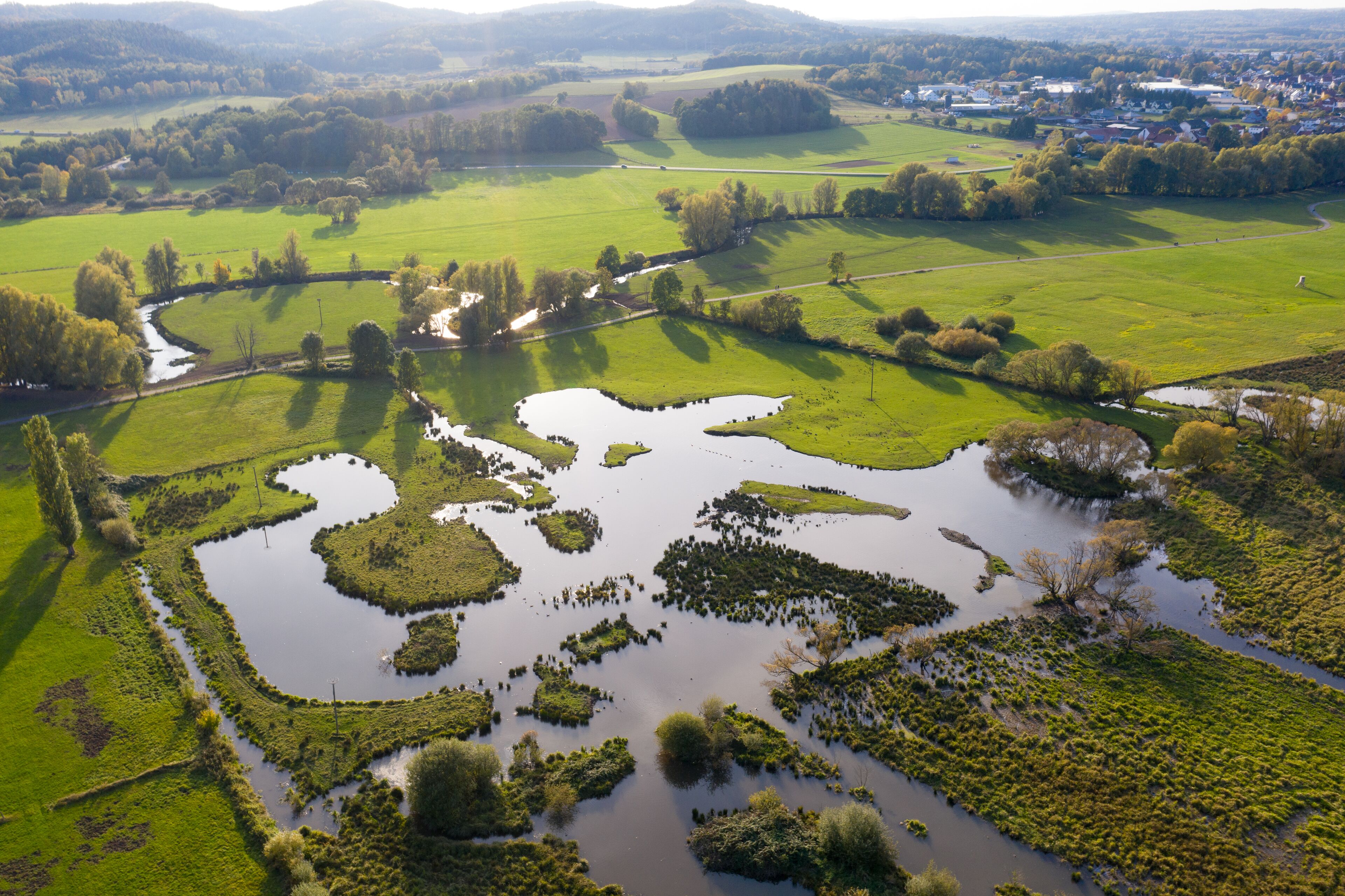 An aerial view of a rural landscape with fields, water bodies, and a small settlement in the distance.