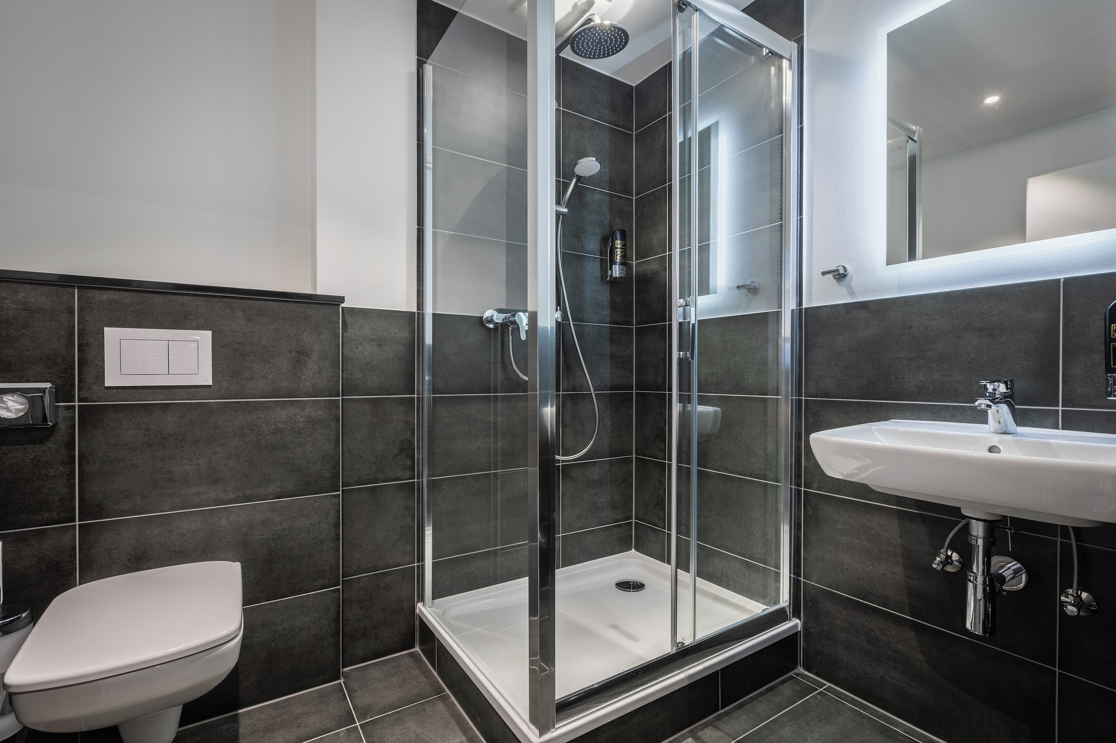 A modern bathroom with a glass-enclosed shower, a white toilet, and a sink with a mirror above it.