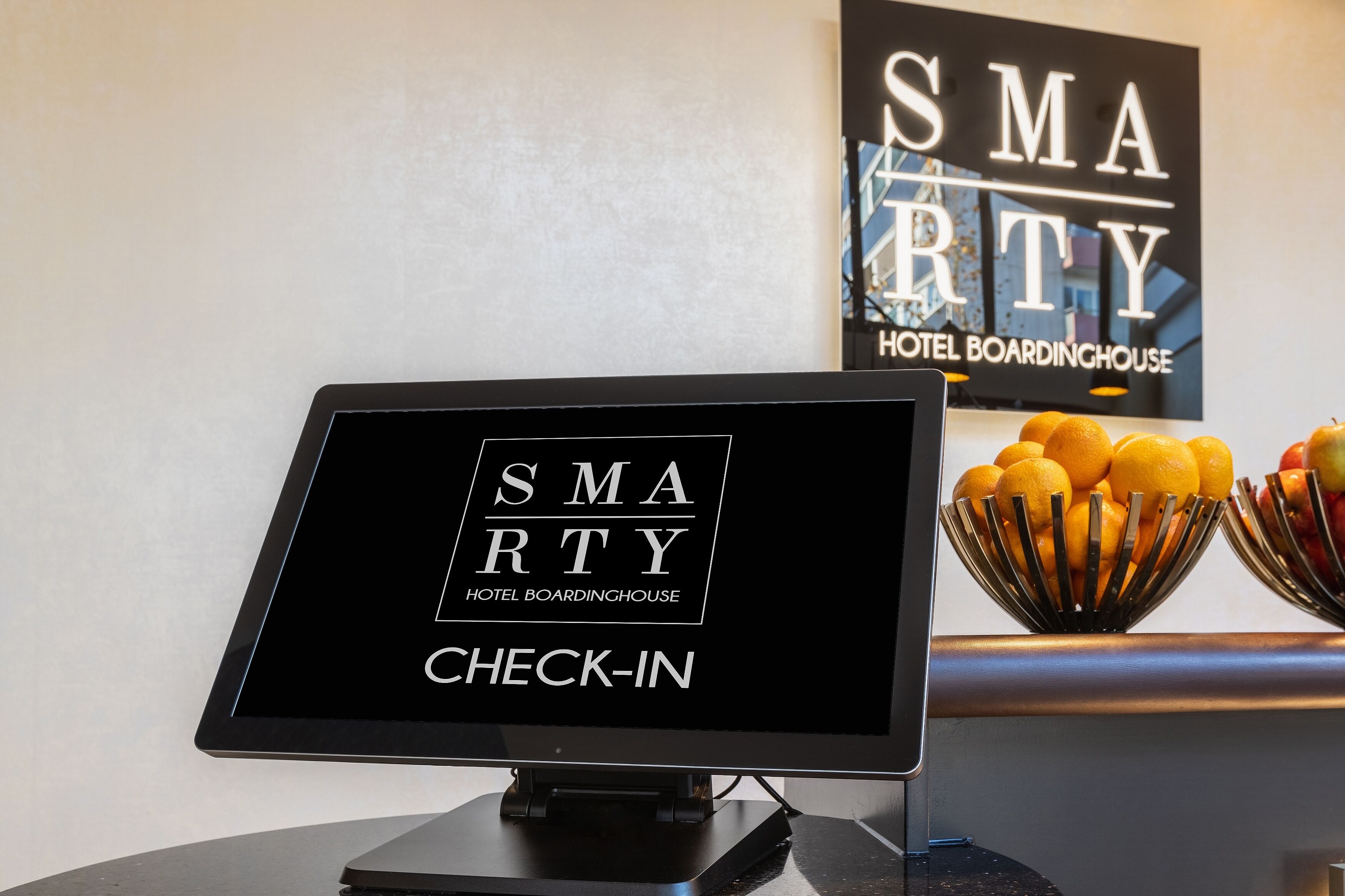 Un quiosco de registro con un cartel que dice "SMARTY HOTEL BOARDINGHOUSE" y un frutero con naranjas y manzanas.