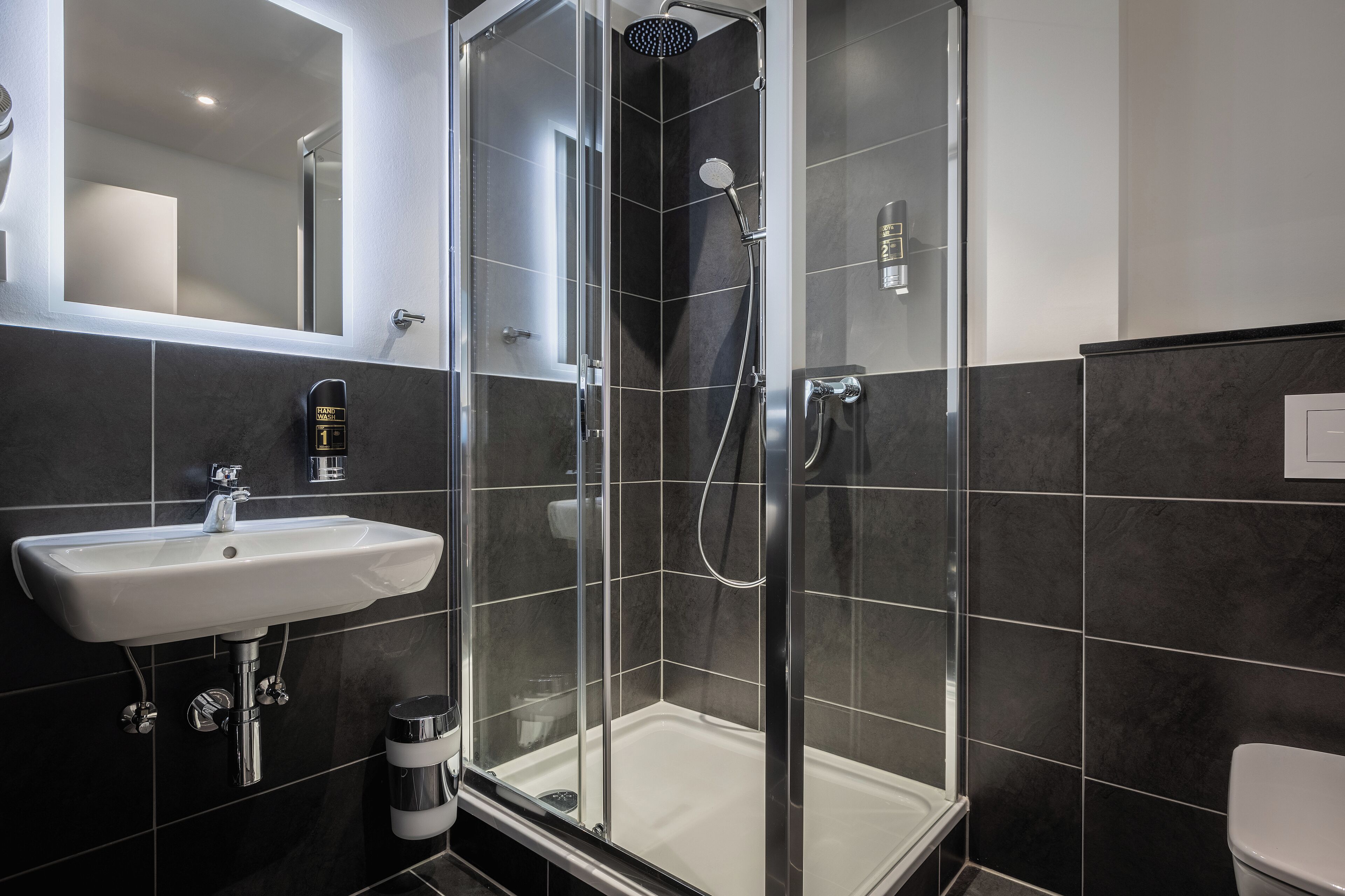 Ein modernes Badezimmer mit einer Duschkabine, einem weißen Waschbecken und einer Toilette.