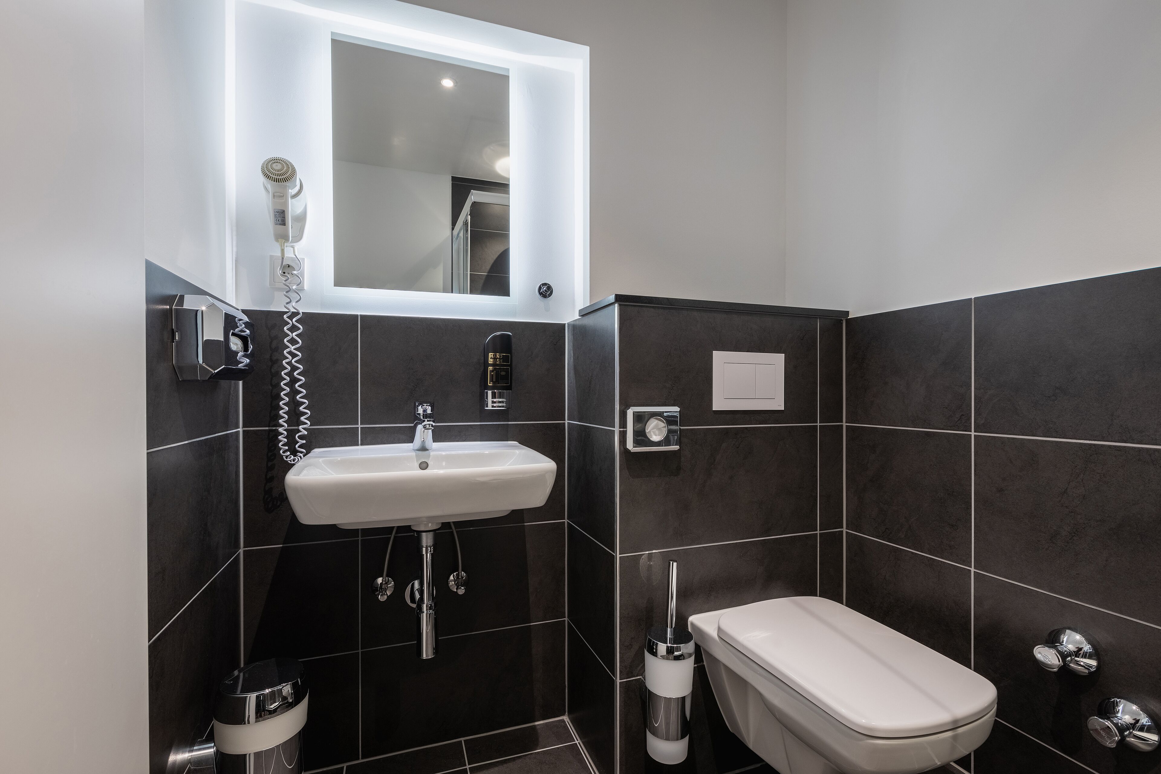 Un baño moderno con lavamanos blanco, secador de pelo y retrete.