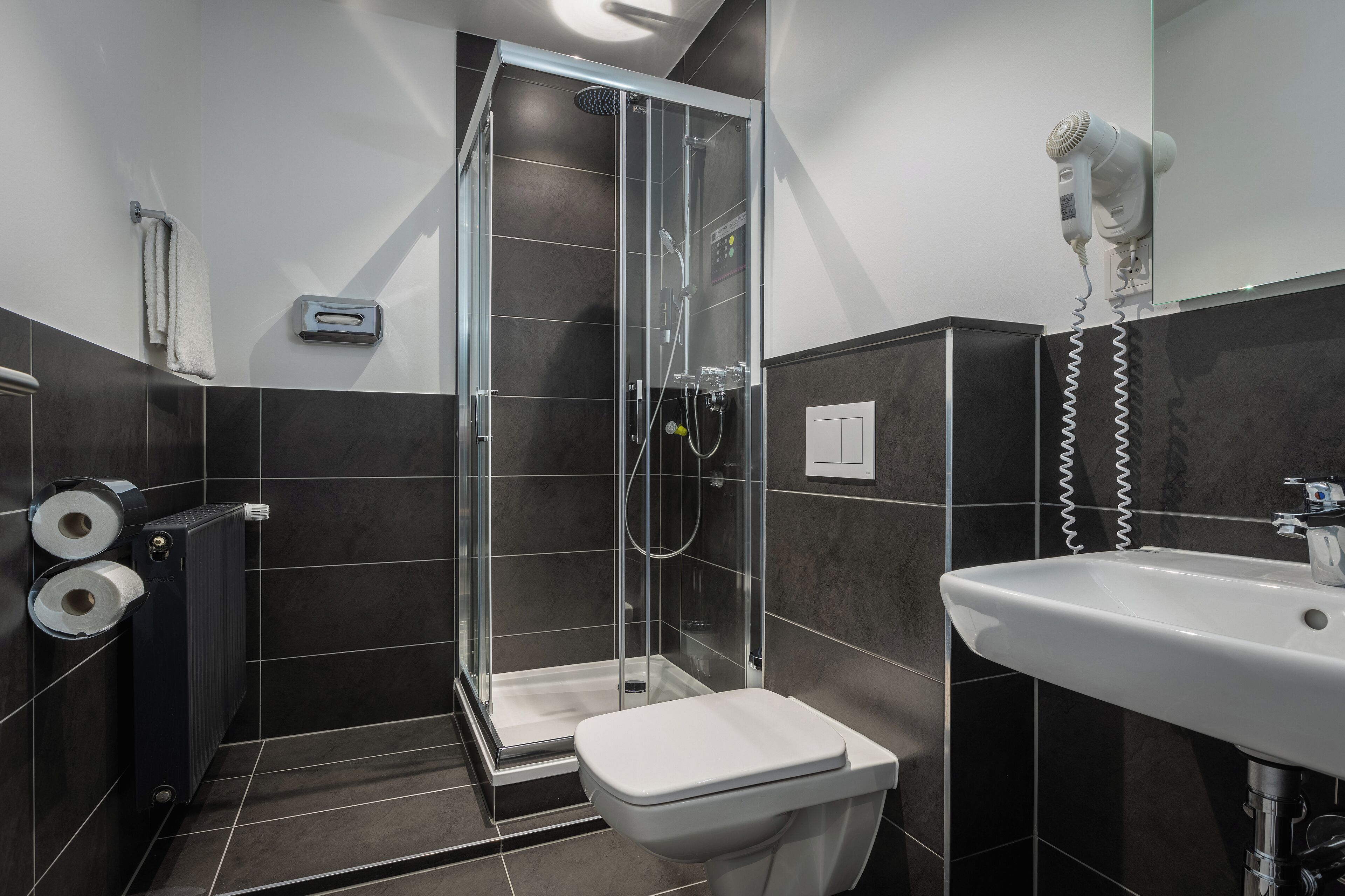 Een moderne badkamer met een douche met glazen wand, een witte wastafel en een aan de muur bevestigde haardroger.