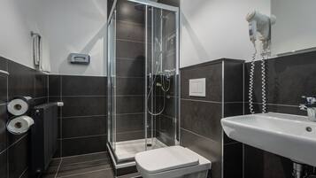 Een moderne badkamer met een douche met glazen wand, een witte wastafel en een aan de muur bevestigde haardroger.