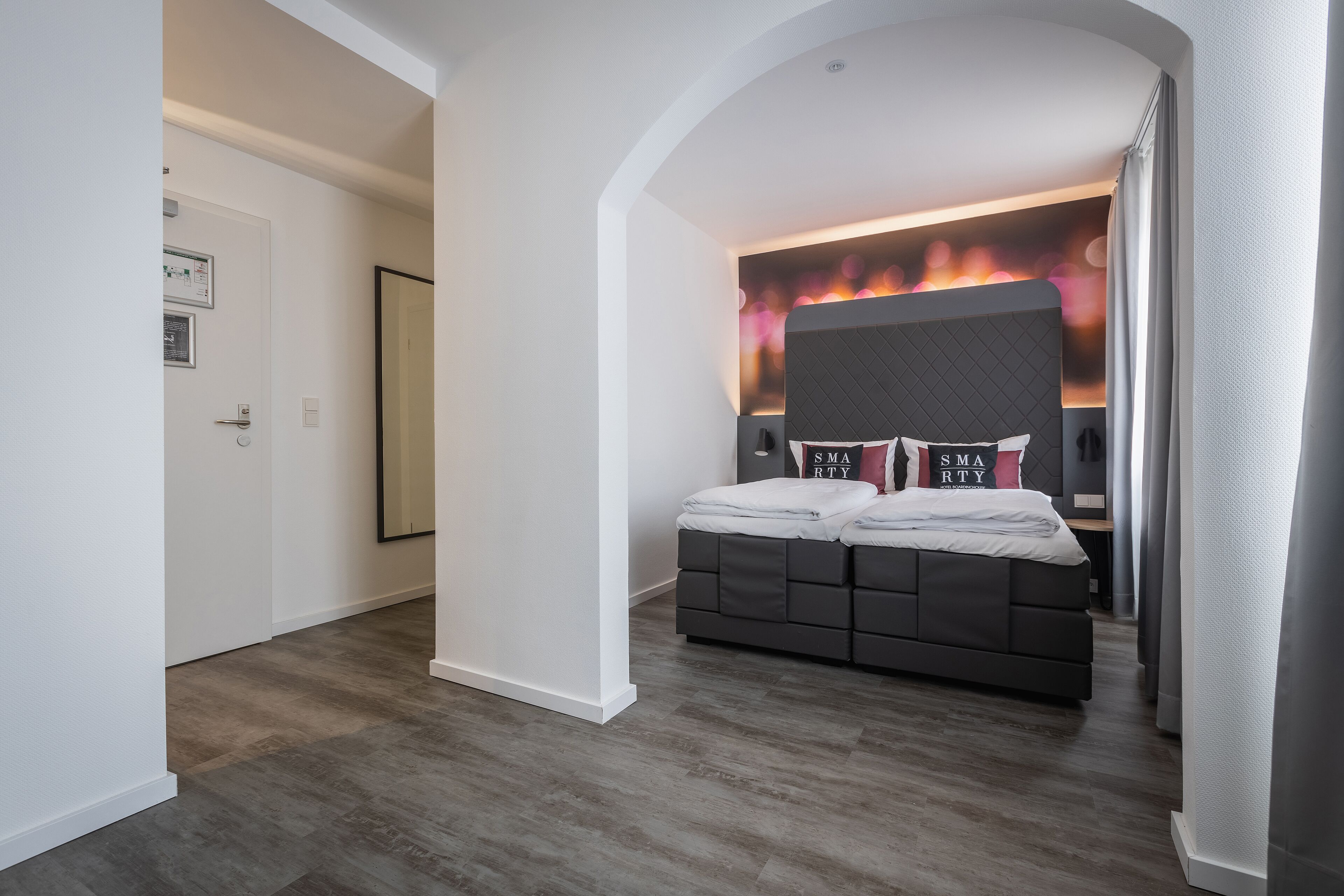 A modern bedroom with a large bed, a headboard with a built-in TV, and a wall-mounted fireplace.