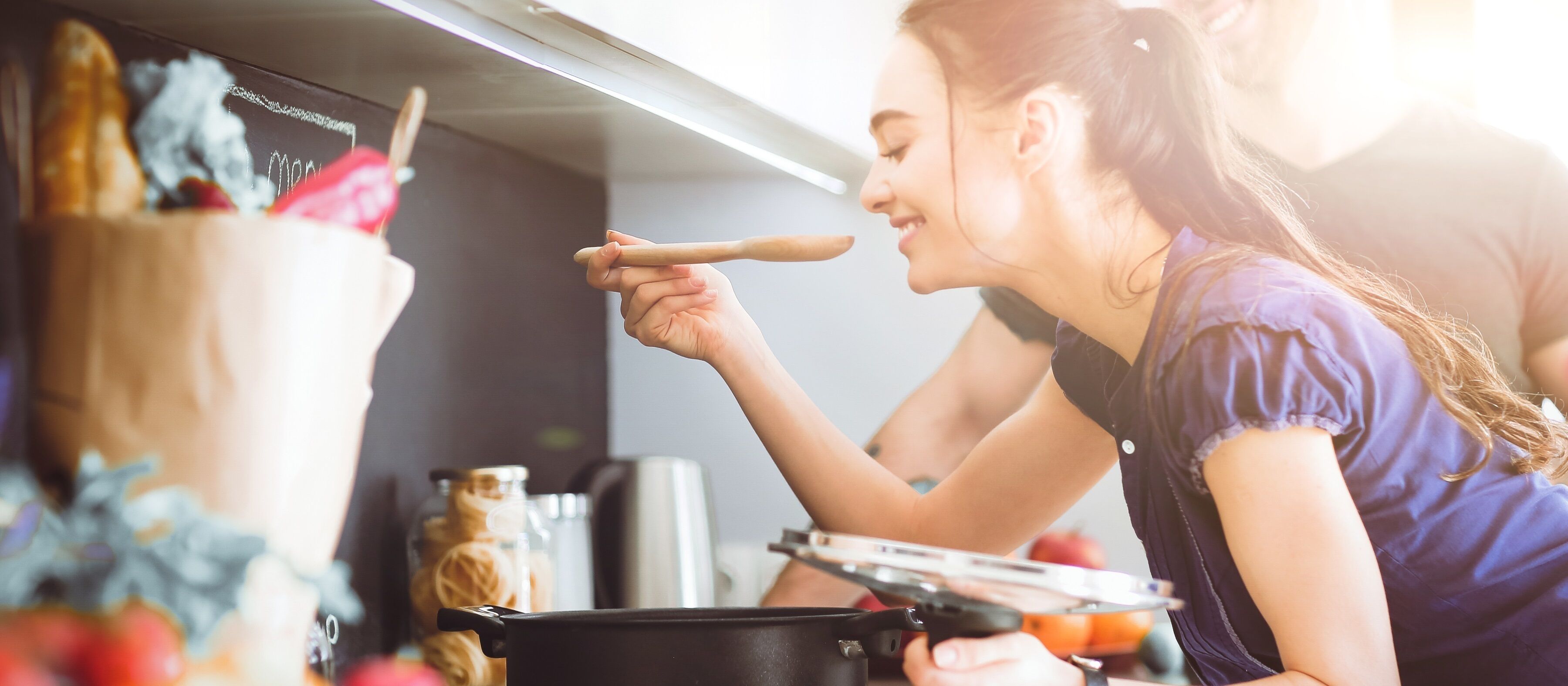 Una persona cocinando con una olla sobre la estufa, un frasco de especias y una cuchara de madera.