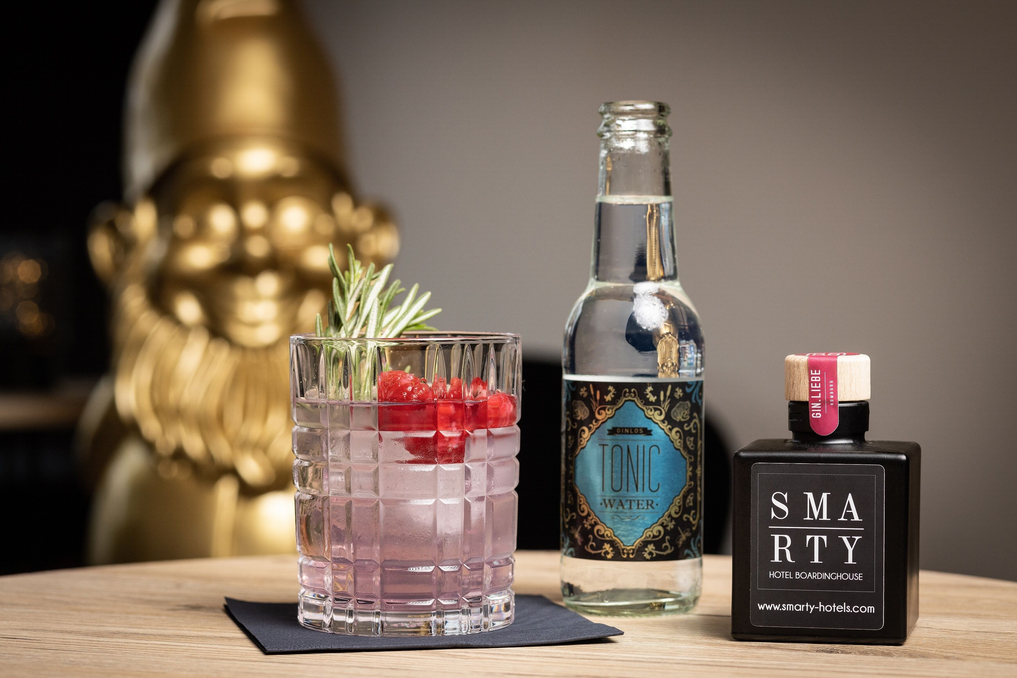 Ein Glas mit einem Getränk, eine Flasche Tonic Water und eine Flasche Ginlikör auf einem Tisch.