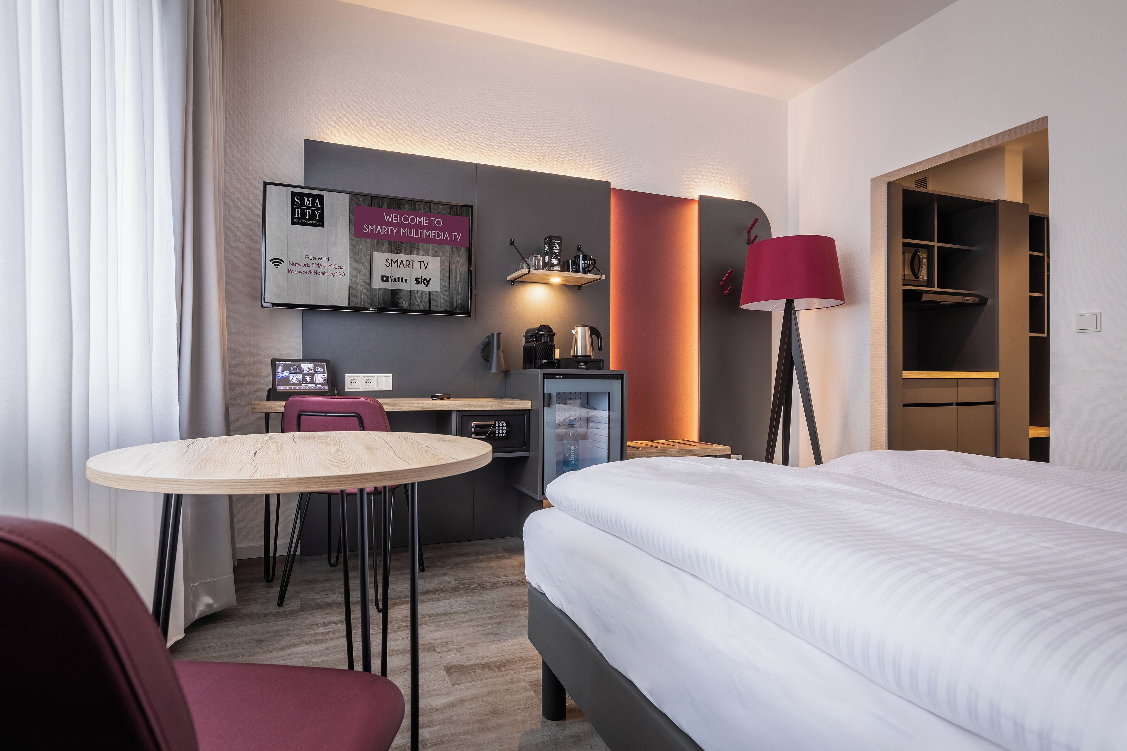 A hotel room with a bed, a desk with a computer, a chair, a lamp, and a TV.