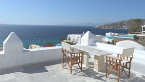 A terrace with a table and chairs overlooking the sea, a pool, and a mountainous landscape. - Villa Amfitriti - Mykonos Guests 6 (Mykonos)