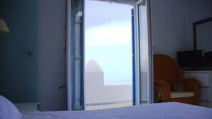A hotel room with a bed, a chair, a television, and a view of the sea through an open door. - Villa Amfitriti - Mykonos Guests 6 (Mykonos)