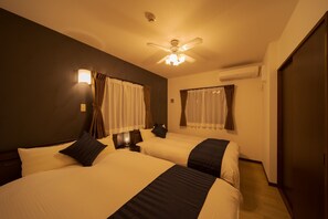 Camera d'albergo con due letti, una ventola a soffitto e un comodino con una lampada.