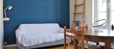 A room with a blue wall, a wooden floor, a white sofa, a wooden dining table, and a chair.