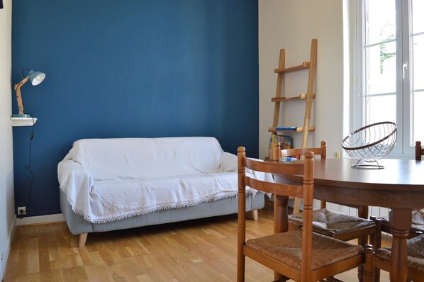 Habitación con pared azul, suelo de madera, sofá blanco, mesa de comedor de madera y una silla.
