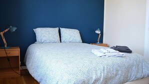 A neatly made bed with a patterned bedspread, two pillows, a bedside lamp, and a folded towel on the nightstand. - 2 steps from the beach - Centre d'Asnelles (Asnelles)