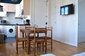 A compact kitchen with a washing machine, a microwave, and a coffee maker. There is a dining table with four wooden chairs and a TV mounted on the wall. - 2 steps from the beach - Centre d'Asnelles (Asnelles)