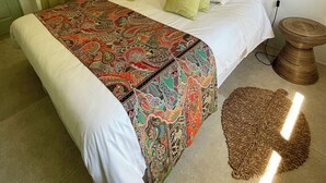 Een slaapkamer met een groot bed, een decoratief hoofdbord, twee bedlampjes en een geweven nachtkastje.