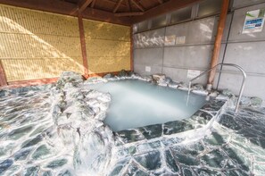 Relax in a serene onsen bath surrounded by a rocky perimeter and natural stone floor.