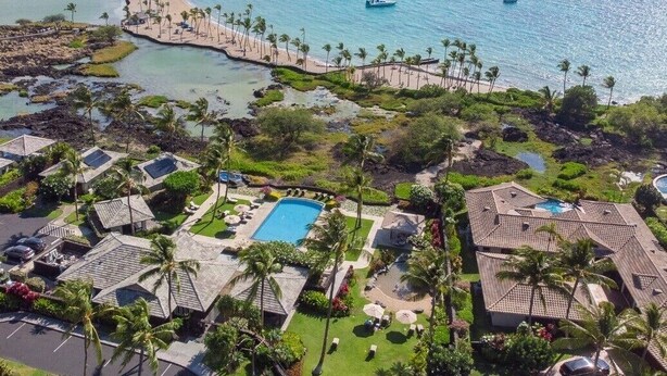 Vista aérea de un complejo turístico con múltiples piscinas, frente a la playa y barcos.