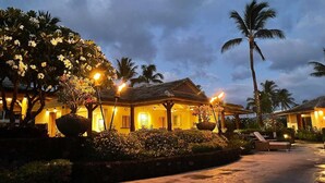 Un resort con un área exterior techada, palmeras y un camino bien iluminado.