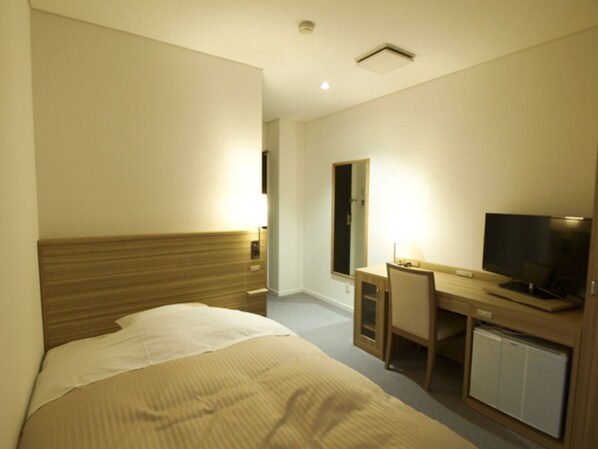 A hotel room with a bed, a desk with a television, and a mirror.
